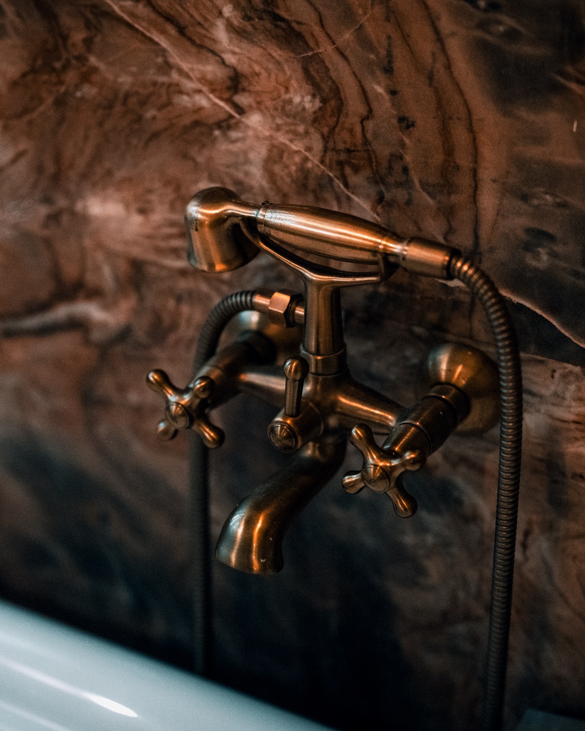 Brass bath mixer and hand-shower against a dark marble wall